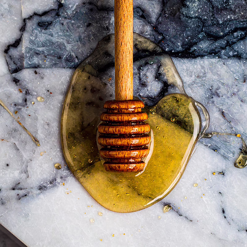 Wooden honey spoon sitting on a bed of runny Manuka honey on marble chopping board