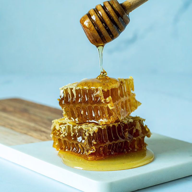Manuka honey from a wooden honey spoon poured over honey combs on wooden and marble chopping board